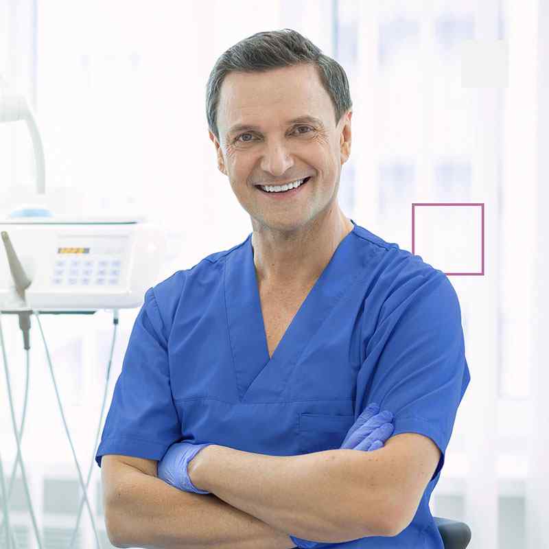 A man in blue scrubs is smiling for the camera.
