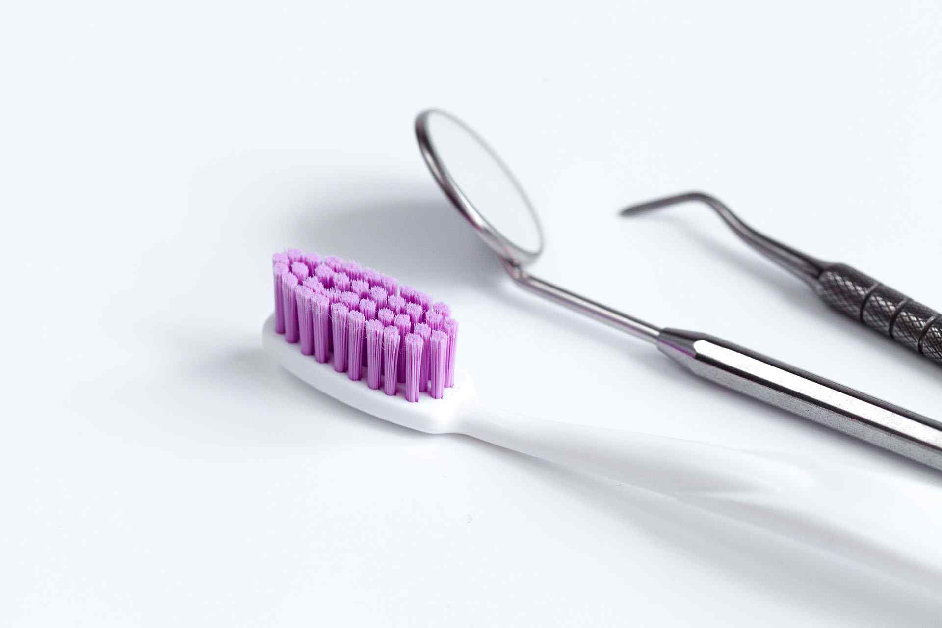 A purple toothbrush and mirror on top of white surface.