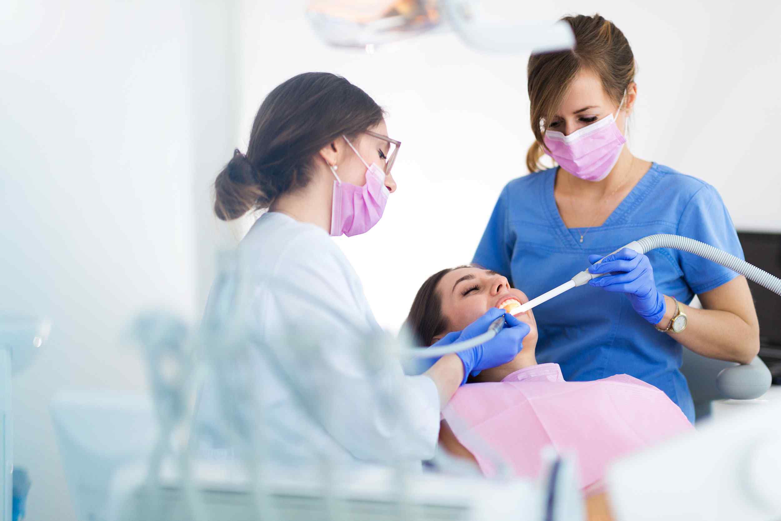 A dentist and two women wearing masks while one of them is holding a tooth brush
