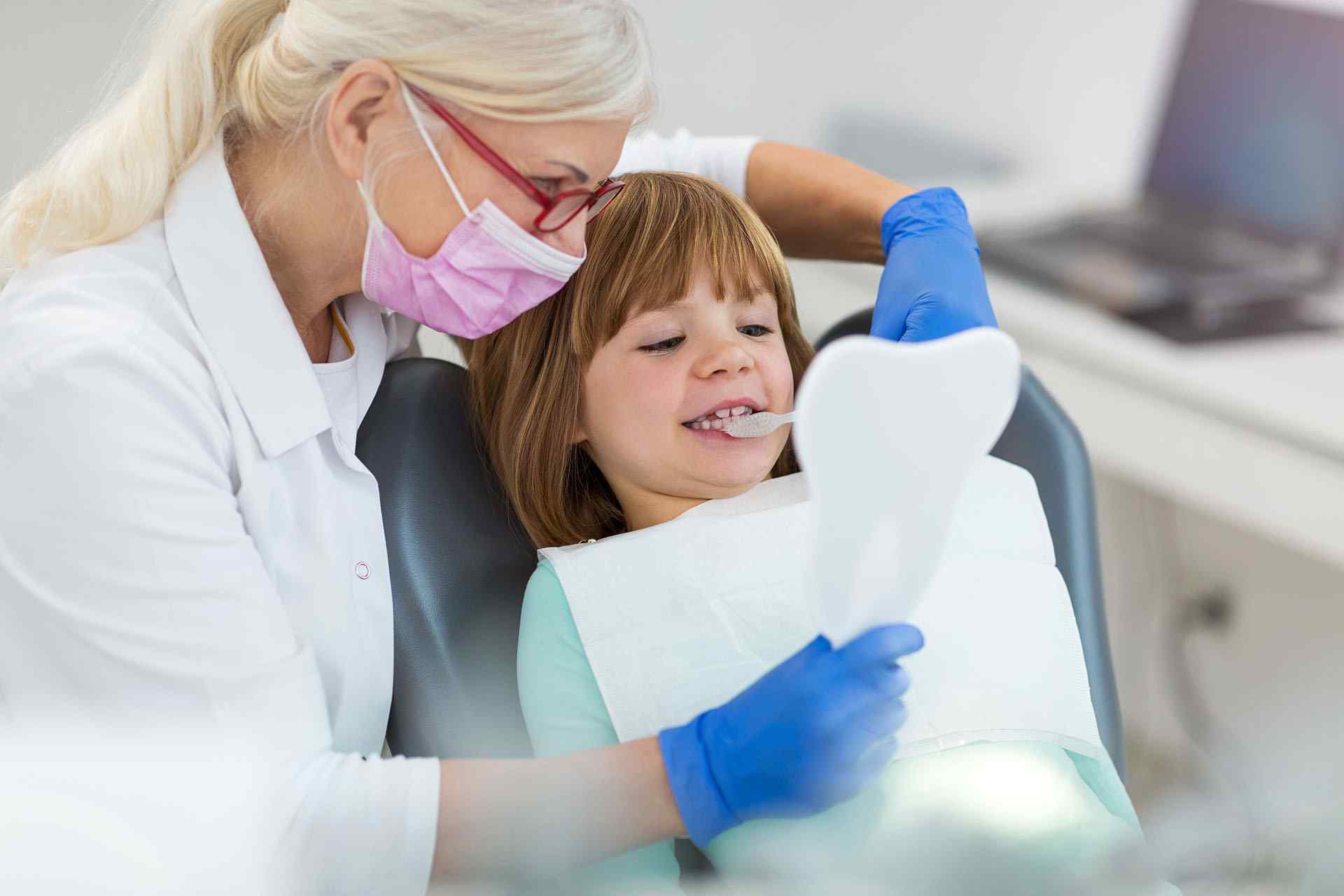 A little girl sitting in the dentist chair with her mom.